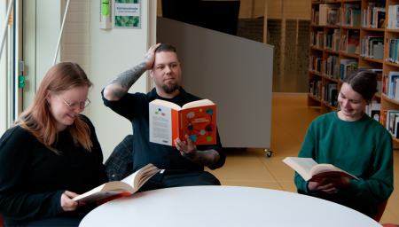 Kolme sosionomin opiskelijaa istuvat pöydän äärellä kirjastossa. Lukevat kirjoja.